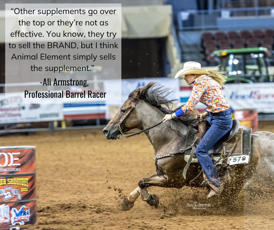A blonde woman riding a roan horse approaching a barrel in an arena.